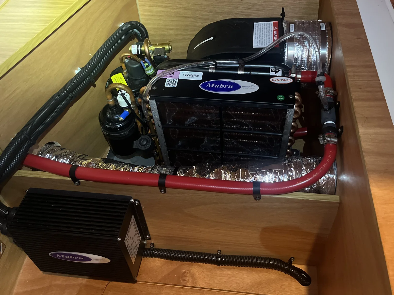 Mabru 12V DC air conditioning unit installed in a joinery locker with insulated ducting and cooling hoses